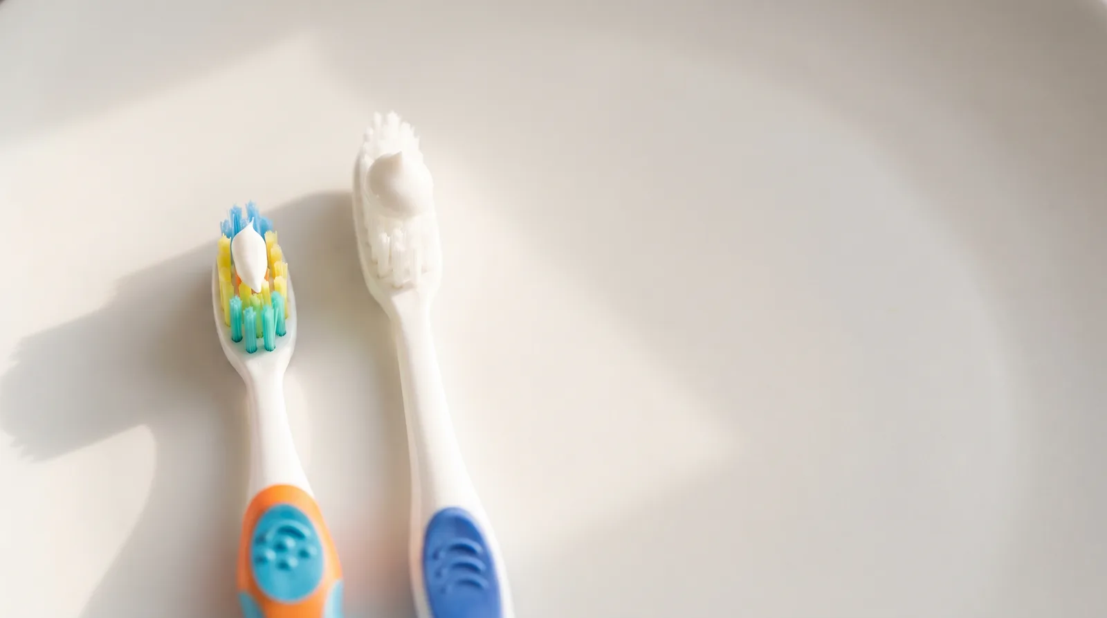 A child's toothbrush with a small smear of toothpaste beside an adult brush with a pea-sized amount