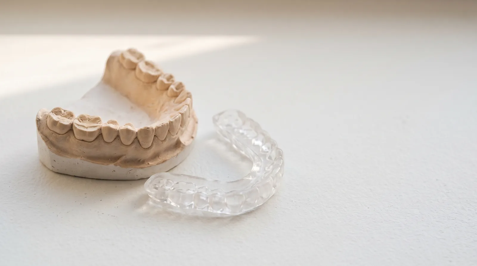 A plaster jaw model with worn biting surfaces beside a clear night guard