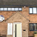 The brick frontage of TG's Dental Suite Scraptoft, with the illuminated roundel above the clinician name-board and front door