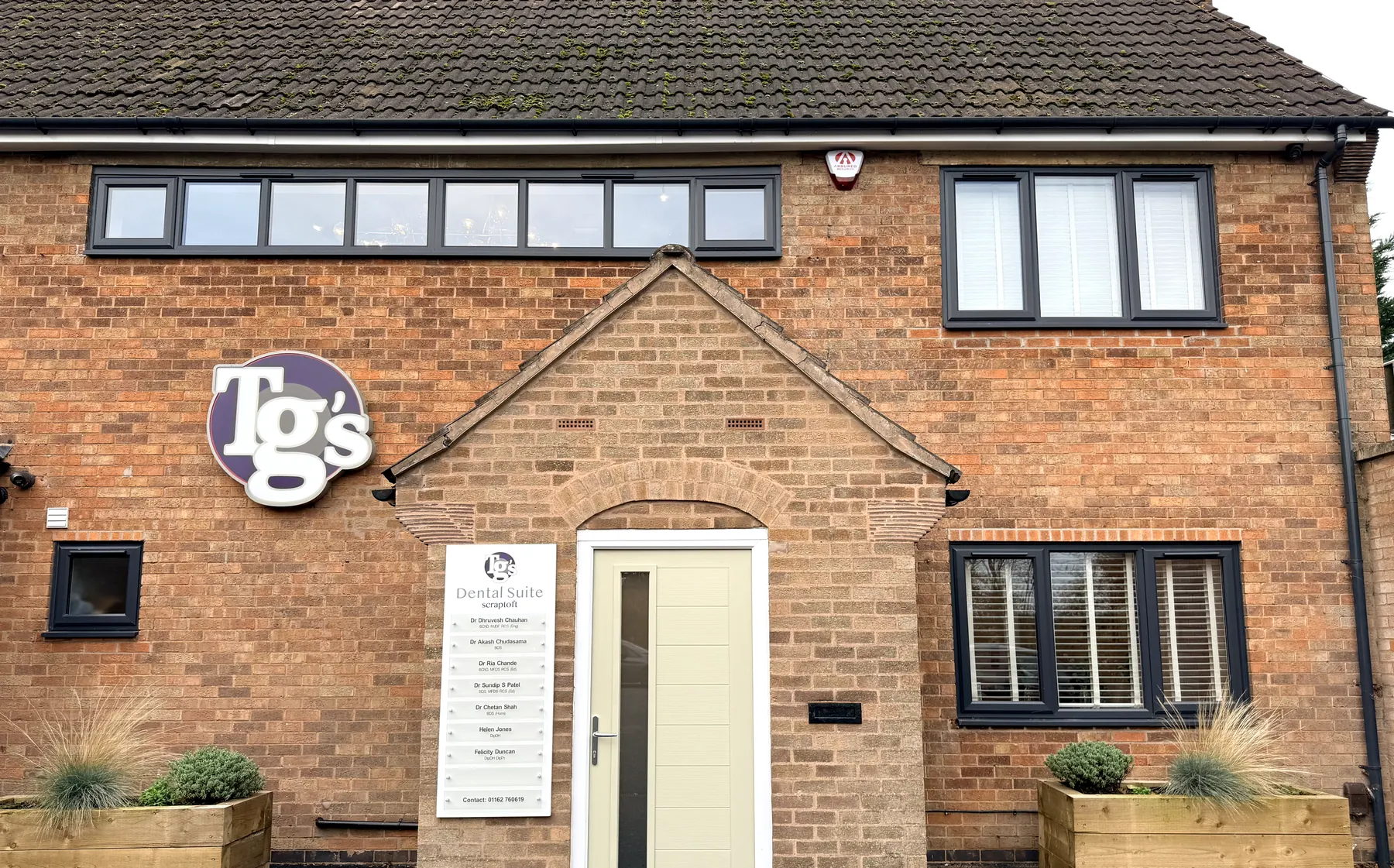 The brick frontage of TG's Dental Suite Scraptoft, with the illuminated roundel above the clinician name-board and front door