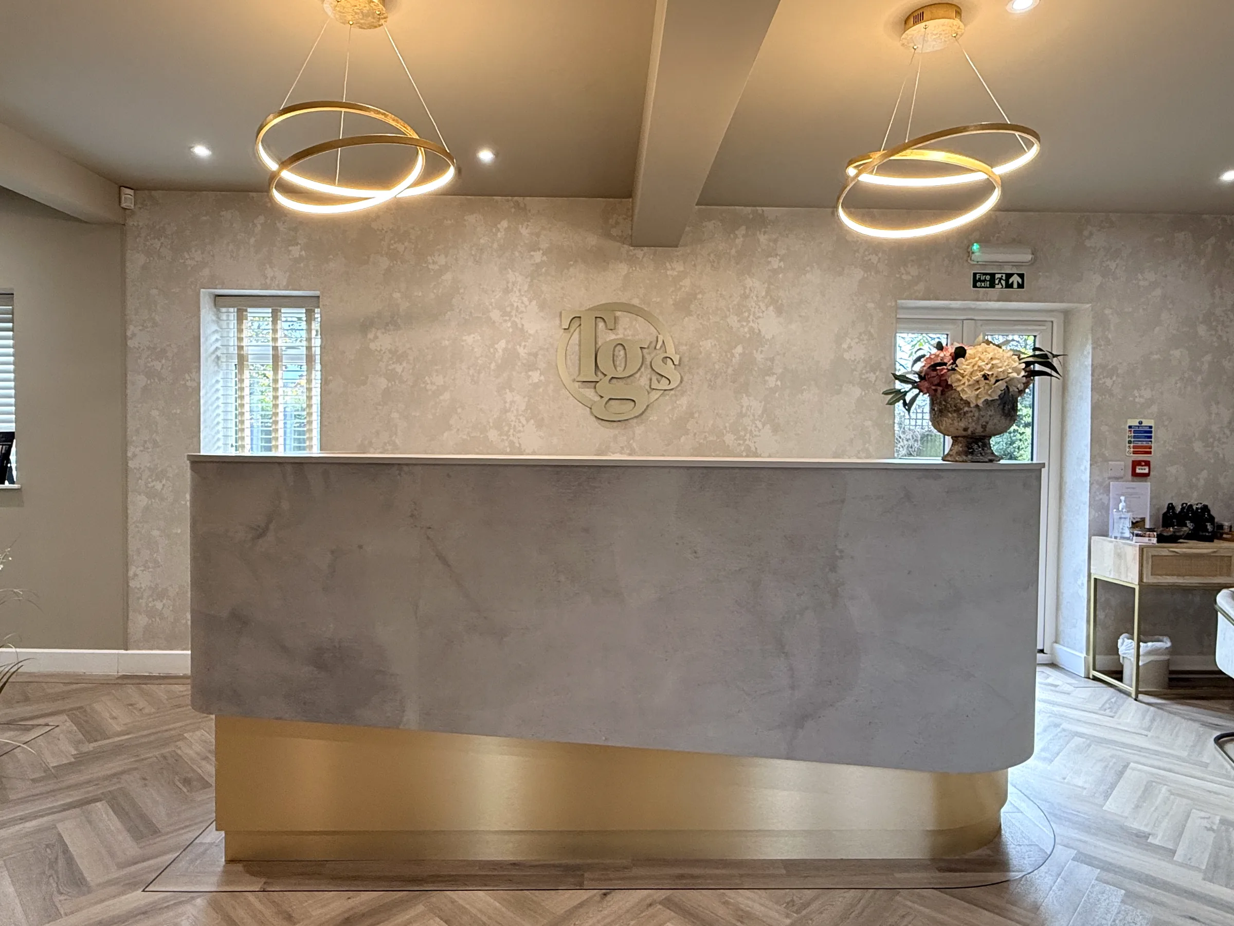 The Scraptoft reception desk under two ring pendants, with the TG's monogram on the wall behind