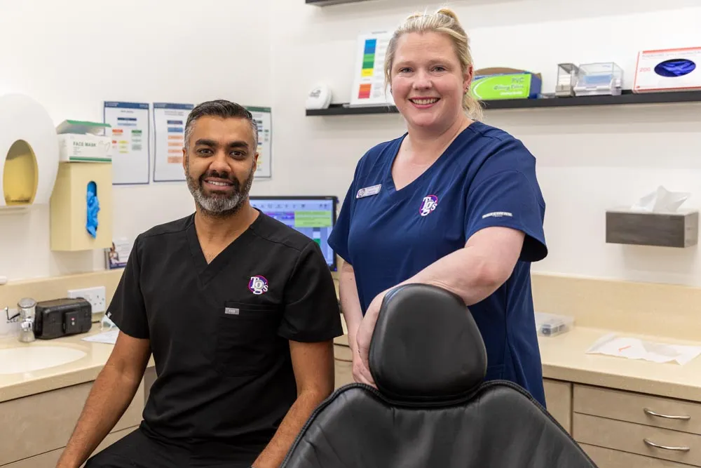 A dentist and dental nurse in TG's Dental Suite branded scrubs standing together in a treatment room