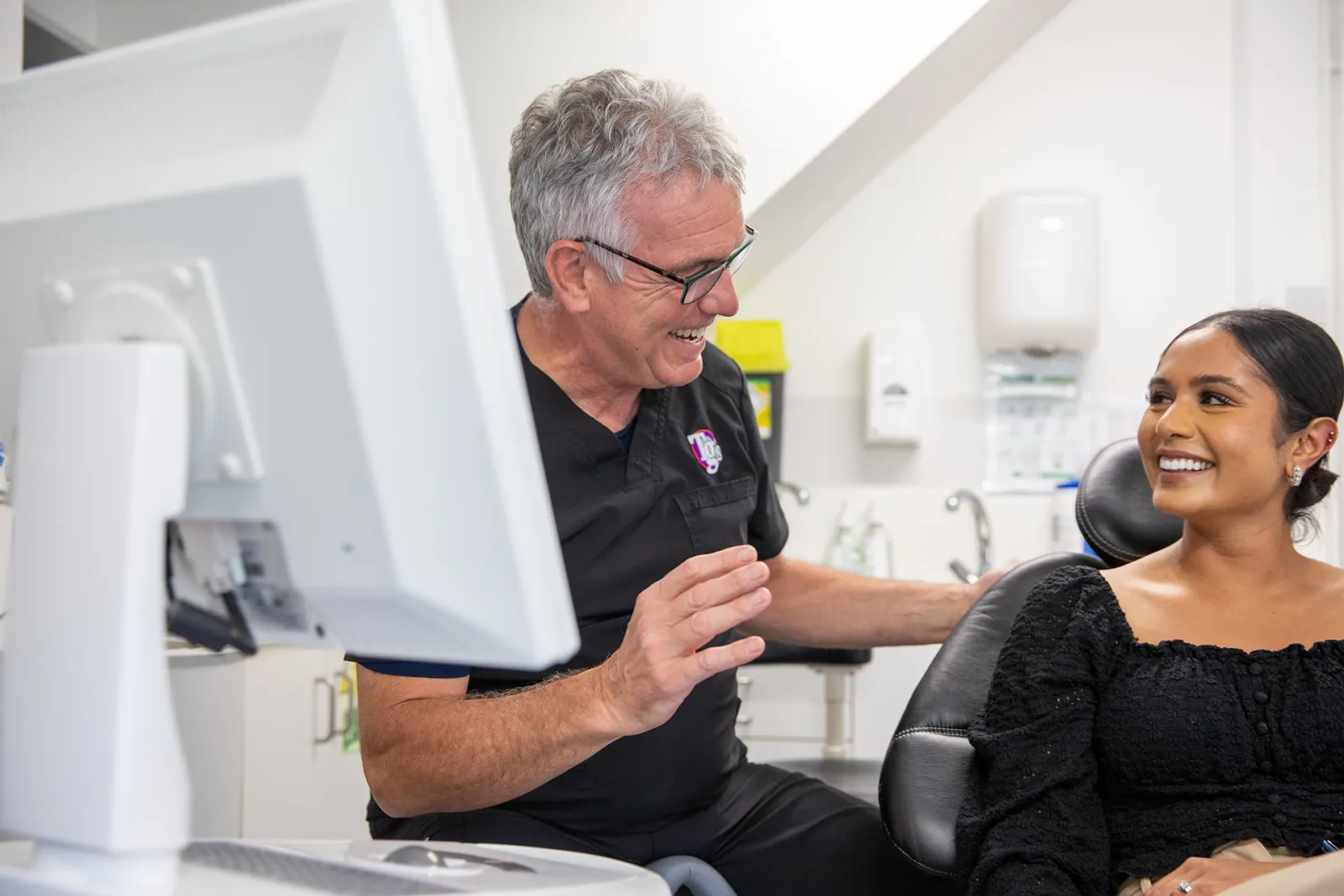 Dentist sharing a laugh with a smiling patient during a consultation in the dental chair